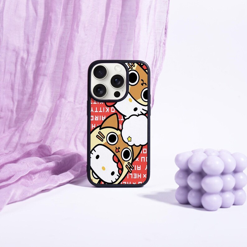 May include: Black phone case featuring a cartoon cat design with a red background. The case has a black border and a design of a cat wearing a costume. The text "HELLO KITTY" is printed vertically on the left side of the case.