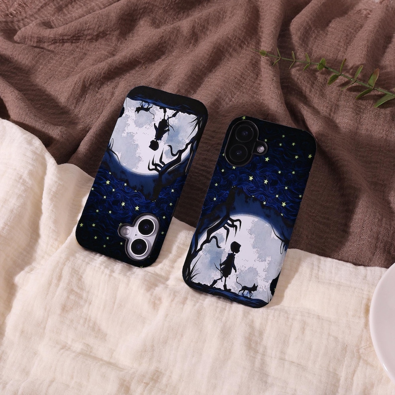May include: Two black phone cases with a dark blue night sky design. The cases feature a full moon, silhouettes of trees, and a figure walking with a cat. The cases have a black border and camera cutouts.