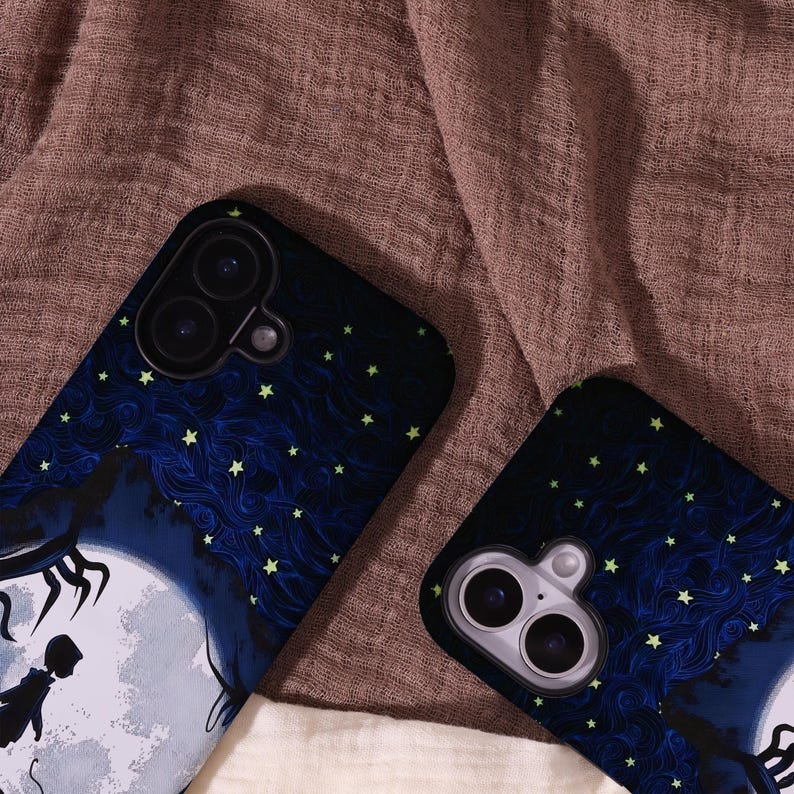 May include: Two phone cases with a dark blue and black design featuring a full moon, silhouette figures, and a starry night sky. The cases have a glossy finish and are set against a brown fabric background.