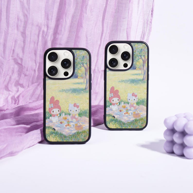 Puede incluir: Dos fundas negras para tel&eacute;fono con una colorida ilustraci&oacute;n de una escena de picnic con personajes de dibujos animados. Las fundas tienen un borde negro y un acabado brillante. El fondo es una tela morada clara y una superficie blanca.