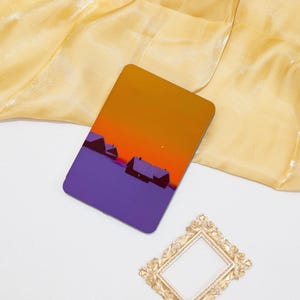 Könnte beinhalten: Eine violette und orangefarbene Illustration einer verschneiten Landschaft mit drei Häusern. Der Himmel ist leuchtend orange und die Häuser sind vor dem Sonnenuntergang silhouettiert.