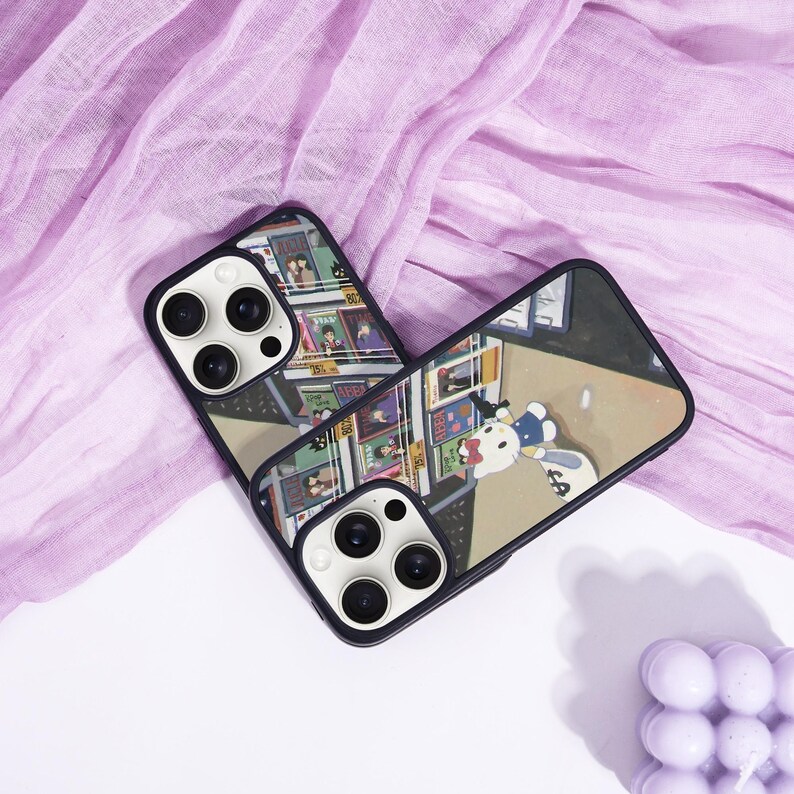 May include: Two black phone cases with a colorful cartoon design. One case features a comic book-style illustration, while the other showcases a cartoon character with a money bag. The cases are set against a purple fabric background.