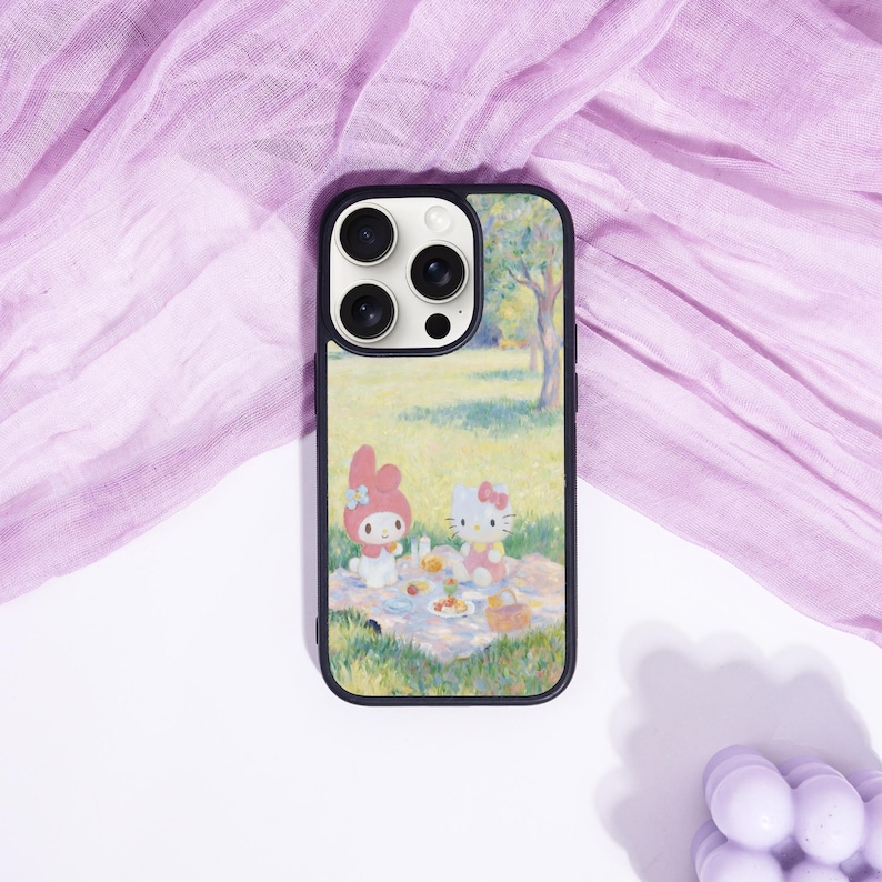 Puede incluir: Funda de tel&eacute;fono negra con una colorida ilustraci&oacute;n de una escena de picnic con dos personajes de dibujos animados. La funda tiene un borde negro y un recorte para la c&aacute;mara. El fondo es una tela morada clara.