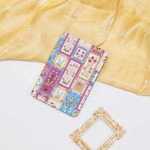 Könnte beinhalten: Ein farbenfrohes Patchwork-Design mit rosa, blauen und weißen Blumen in einem quadratischen Muster. Das Design ist auf einem cremefarbenen Hintergrund.