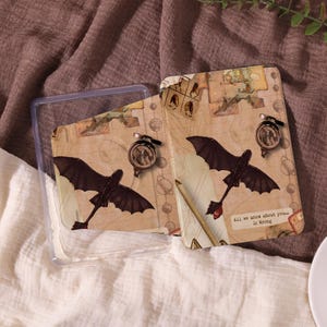 May include: Two decorative cards with a dragon design and a small compass. The cards are tan with a map design and the text "All we know about you... is Wrong". The cards are in a clear plastic case.