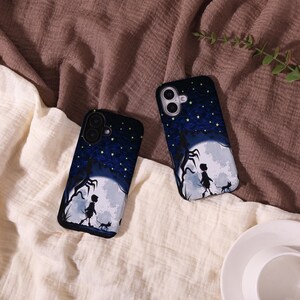 May include: Two black phone cases with a dark blue night sky design. The cases feature a silhouette of a person walking with a cat in front of a full moon. The cases have a starry night design.