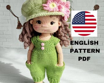 Puede incluir: Muñeca de ganchillo hecha a mano con un mono verde, zapatos a juego y un sombrero verde claro adornado con una flor rosa. La muñeca tiene cabello rizado castaño y una expresión dulce. La imagen incluye el texto "ENGLISH PATTERN PDF" y una bandera americana.
