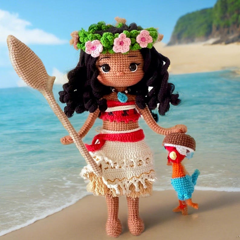 Op de afbeelding: Een gehaakte pop van Moana uit de Disney-film Vaiana, met een bloemenkroon, een rood-wit topje en een witte rok met een bruine franje. Ze houdt een bruin houten peddel vast en een klein gehaakt blauw-oranje vogeltje.