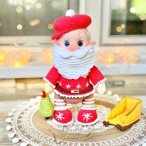 Puede incluir: Mu&ntilde;eco de ganchillo hecho a mano de Pap&aacute; Noel. El mu&ntilde;eco lleva un gorro, una chaqueta y botas rojas, y tiene una barba blanca. Sostiene un &aacute;rbol de Navidad verde. Un trineo amarillo est&aacute; al lado del mu&ntilde;eco.