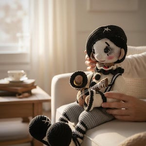 May include: A handmade crochet doll dressed as a musician, wearing a black beret with a white star, a white and black outfit, and striped gray pants. The doll is holding a small brown instrument with strings.