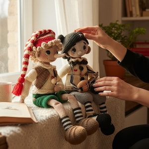May include: Two handmade crochet dolls, one with a red and white striped hat and the other with a black hat. The dolls are sitting on a window sill. The doll on the left has a long nose, green shorts, and a brown vest.