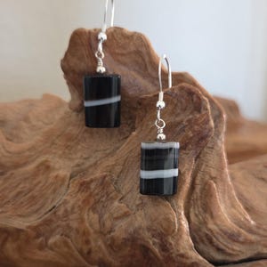 May include: A pair of dangle earrings featuring rectangular black glass beads with horizontal white stripes. The beads are suspended from silver-toned metal ear wires, each accented with a small silver-toned bead at the top of the glass component.