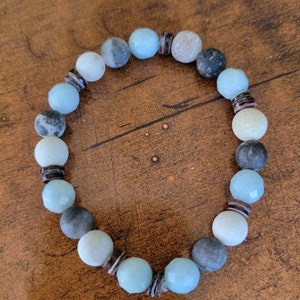 May include: A blue and gray beaded bracelet with brown spacers. The beads are round and have a smooth, polished finish.