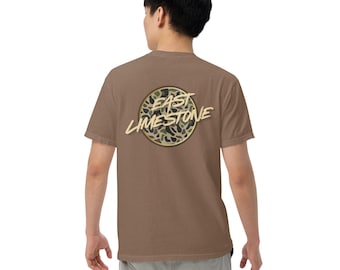 May include: A brown t-shirt with the text "East Limestone" in a gold, stylized font, set within a circular design. The design features a camouflage pattern in shades of green and brown. The shirt is a short-sleeved, casual style.