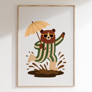 Puede incluir: Un oso marrón con pijama a rayas verdes y blancas y gafas de sol salta en un charco de barro. El oso sostiene una sombrilla amarilla.