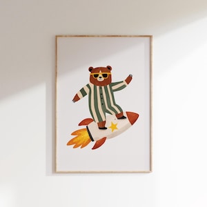 May include: Framed art print showing a cartoon bear in sunglasses and a green and white striped jumpsuit, riding a rocket. The rocket has a yellow star and orange flames. The artwork is set against a white background.