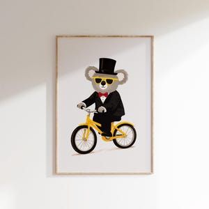 Puede incluir: Impresión enmarcada que presenta un koala con esmoquin negro, sombrero de copa y gafas de sol amarillas, montando en bicicleta amarilla. El koala lleva una pajarita roja. La obra está sobre un fondo blanco.