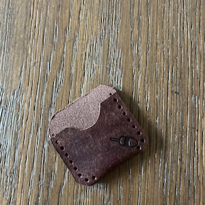 May include: A brown leather wallet with a stitched edge and a small, embossed design.