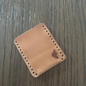 May include: A light brown leather wallet with a stitched edge and a small logo embossed on the front.