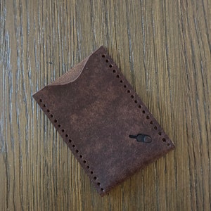 May include: A brown leather wallet with a stitched edge and a small hole for a key ring.