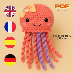 Pode incluir: Um brinquedo de amigurumi de água-viva de crochê com um corpo rosa, tentáculos roxos e um laço amarelo. O brinquedo tem aproximadamente 38 cm de altura. Padrão PDF.