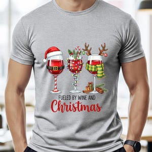 Peut inclure: T-shirt gris avec un motif de No&euml;l. Il pr&eacute;sente trois verres &agrave; vin d&eacute;cor&eacute;s pour les f&ecirc;tes, avec un bonnet de P&egrave;re No&euml;l, des lumi&egrave;res et des bois de renne. Le texte "Fueled by Wine and Christmas" est imprim&eacute; en rouge en dessous.