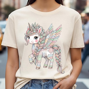 May include: A beige t-shirt featuring a colorful illustration of a unicorn with a patchwork design. The unicorn has a horn, wings, and a long braided mane and tail. The design incorporates pastel colors and floral accents.