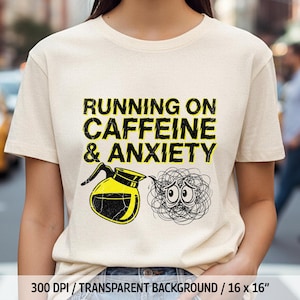May include: A cream-colored t-shirt with the text "RUNNING ON CAFFEINE & ANXIETY" in black and yellow. The graphic includes a coffee pot and a tangled ball with eyes. The shirt is a standard crew neck.