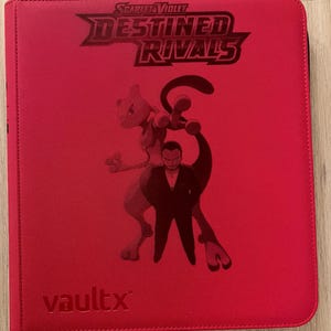 Peut inclure: Classeur rouge Vault X avec le texte "Scarlet & Violet Destined Rivals" et un graphisme d'un personnage Pokémon et d'une personne en costume. Le classeur est pour les cartes à collectionner.
