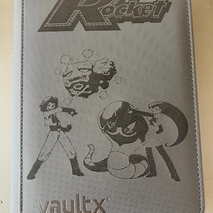 May include: Gray card binder featuring the text "Team Rocket" and various character illustrations. The binder has a textured surface and the brand name "vaultx" is visible at the bottom.