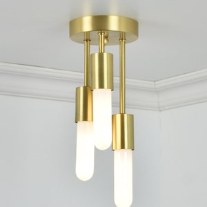 May include: A gold ceiling light fixture with three cylindrical bulbs. The bulbs are frosted glass and emit a warm white light.