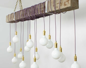 Op de afbeelding: Een rustieke houten balk-kroonluchter met meerdere witte bolvormige lampen die aan paarse snoeren hangen. De kroonluchter is met messing kettingen aan het plafond gehangen.