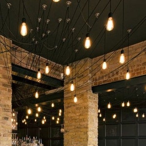 May include: A dark wood bar with a black countertop and black cabinets. The bar is lit by a series of exposed Edison bulbs hanging from the ceiling. The walls are made of exposed brick.