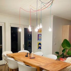 May include: A wooden dining table with white chairs and a set of colorful pendant lights hanging above. The table is set with a vase of flowers and a candle.