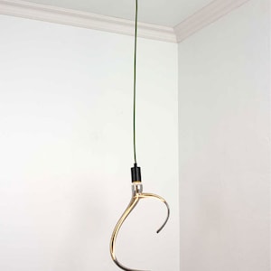 K&ouml;nnte beinhalten: Eine goldfarbene, gebogene Pendelleuchte h&auml;ngt an einem gr&uuml;nen Kabel und einer schwarzen Deckenhalterung. Die Gl&uuml;hbirne ist astf&ouml;rmig.