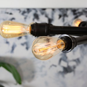 Może przedstawiać: Czarny metalowy żyrandol z czterema odsłoniętymi żar&oacute;wkami Edison. Żyrandol jest zawieszony na suficie i jest oświetlony.