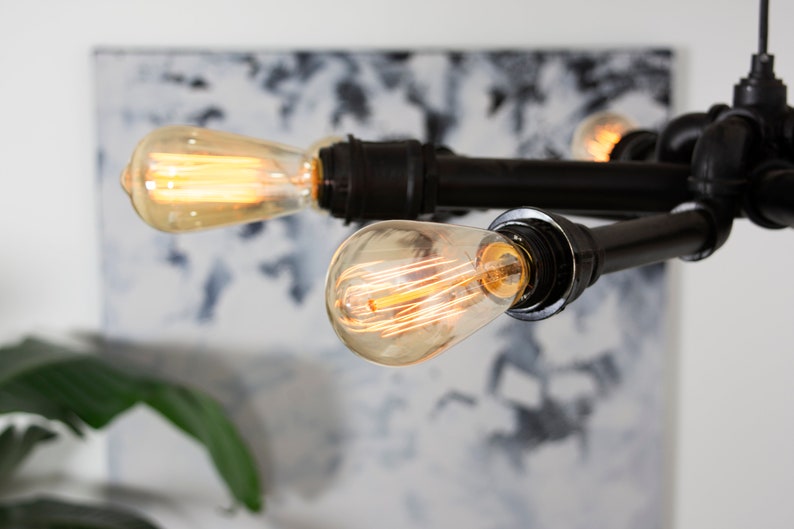 Może przedstawiać: Czarny metalowy żyrandol z czterema odsłoniętymi żar&oacute;wkami Edison. Żyrandol jest zawieszony na suficie i jest oświetlony.