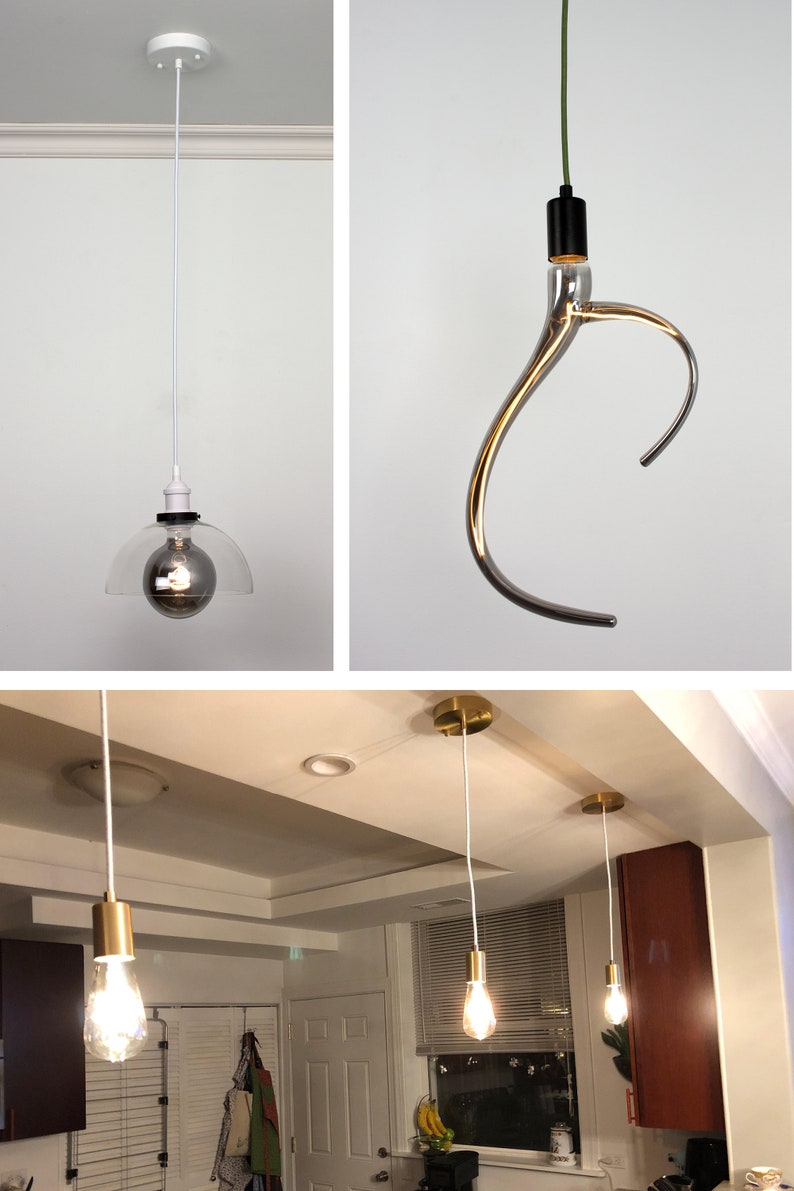 May include: Three different pendant lights with white cords. The first light has a clear glass shade with a silver bulb. The second light has a silver, curved, glass shade with a black cord. The third light has a gold metal shade with a white cord. The lights are hanging from a white ceiling.