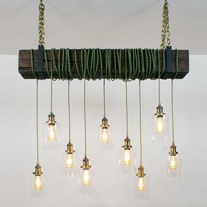 May include: A rustic wooden beam chandelier with nine clear glass pendant lights and green cords. The lights are suspended from the beam with brass chains and fixtures.