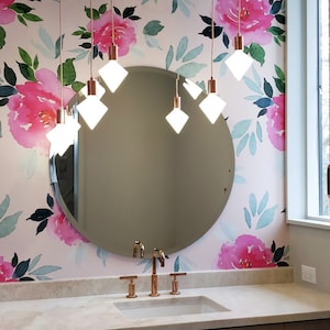 K&ouml;nnte beinhalten: Ein Badezimmer-Waschtisch mit einem runden Spiegel und einer floralen Tapete mit rosa Blumen und gr&uuml;nen Bl&auml;ttern. Der Waschtisch hat eine wei&szlig;e Arbeitsplatte mit einem Waschbecken und einem Satz Kupferarmaturen. Der Spiegel wird von einem Kronleuchter mit sechs Gl&uuml;hbirnen beleuchtet.