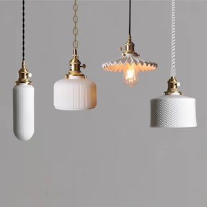 May include: Four white ceramic pendant lights with different designs. The lights have brass fixtures and are hanging from cords or chains.