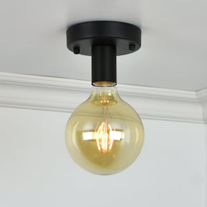 Peut inclure: Un luminaire de plafond noir avec une ampoule ronde en verre dépoli. La lumière est allumée et l'ampoule émet une lueur jaune chaude.