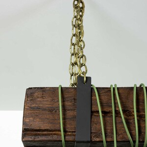 May include: A rustic wooden beam pendant light fixture with a black metal strap and a brass chain hanging from the ceiling. The fixture has green electrical cord wrapped around it.