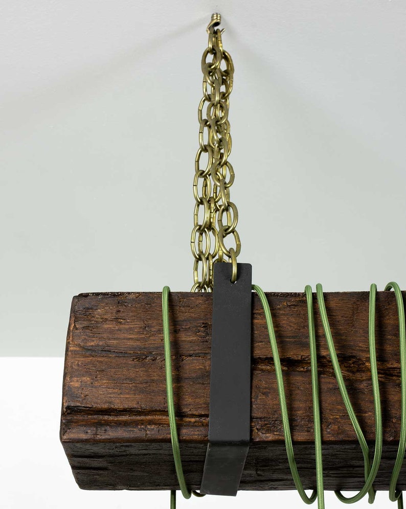 May include: A rustic wooden beam pendant light fixture with a black metal strap and a brass chain hanging from the ceiling. The fixture has green electrical cord wrapped around it.
