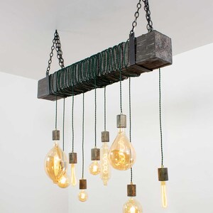 May include: A rustic wooden chandelier with a dark gray finish and multiple Edison bulbs hanging from it. The bulbs are suspended from the wood beam by green cords.