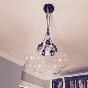 May include: A modern chandelier with six clear glass globe light bulbs hanging from a black ceiling fixture. The bulbs are connected by silver cords.