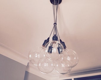 May include: A modern chandelier with six clear glass globe light bulbs hanging from a black ceiling fixture. The bulbs are connected by silver cords.
