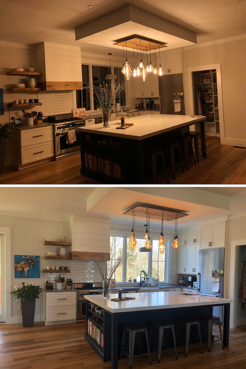 May include: A kitchen island with a white countertop and a dark blue base. The island has open shelving on the side and four metal bar stools. The island is lit by a rustic wood and metal chandelier with Edison bulb lights.
