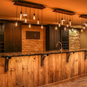 May include: A rustic wooden bar with a granite countertop and a dark brown wood cabinet behind it. The bar is lit by multiple hanging Edison bulb lights.