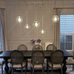Pode incluir: Uma sala de jantar com uma mesa de madeira preta e seis cadeiras. A mesa tem um conjunto de cinco luzes pendentes de globo de vidro transparente penduradas sobre ela.